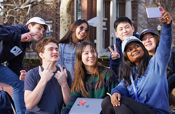 Seven seated smiling students taking a selfie